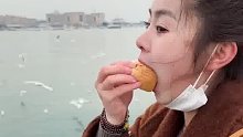 女生拿着烤肠面包去海边喂海鸥，最后自己吃饱了