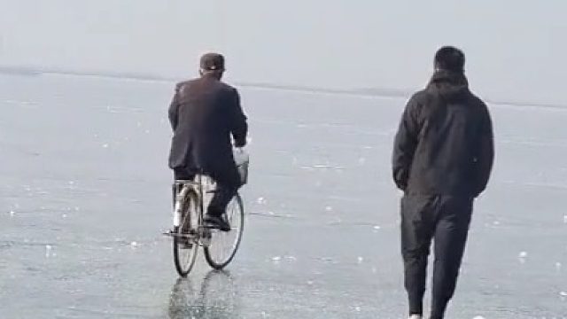 大爷在冰面上骑自行车，最后消失在大家视野里，拍摄者：劝阻了但大爷没理