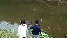 两口子在河边在一起钓鱼，一条大鱼缓缓游过来