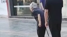 老母亲前面拄拐散步，儿子紧随后面为她扇风