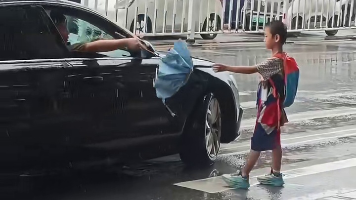 男孩淋着雨站在斑马线上，热心男子主动送上雨伞给男孩遮挡1