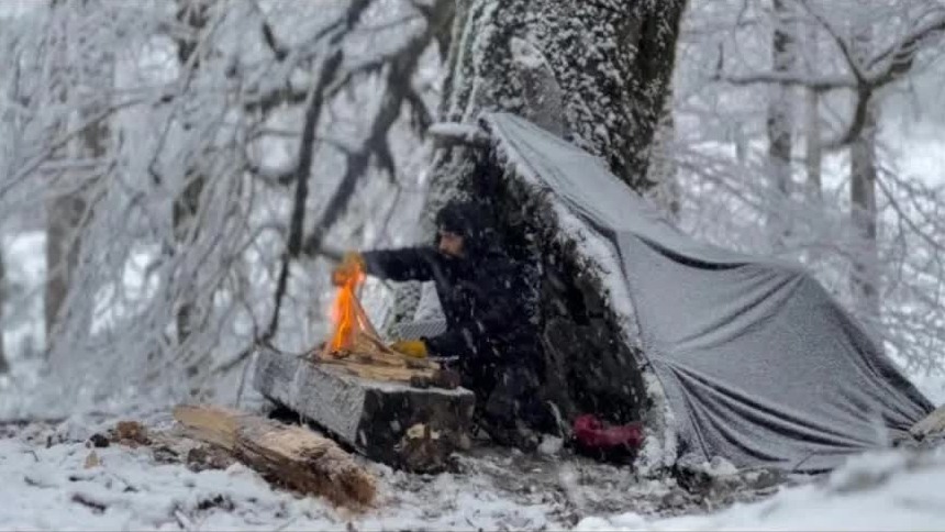 小伙野外露营遭遇暴风雪突袭，利用大树搭建避难所，全靠火堆续命