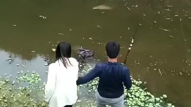 两口子在河边在一起钓鱼，一条大鱼缓缓游过来