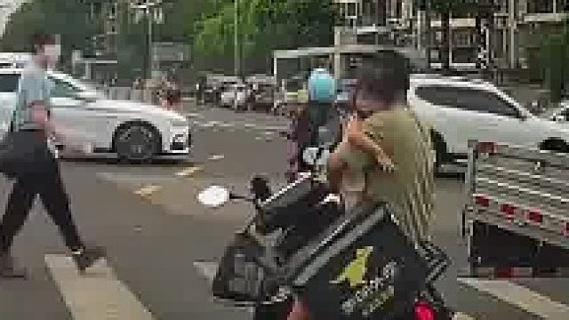 外卖小哥一手抱孩子一手骑电动车，没停好电动车摔倒，随后女子急忙跑过去帮忙​