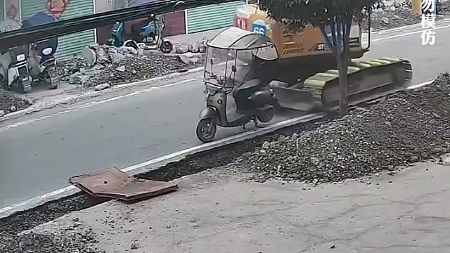 挖机在街上工作时看不到后面的电动车，把电动车撞翻直接掉进沟里，网友:把司机吓坏了 履带下可千万别有人